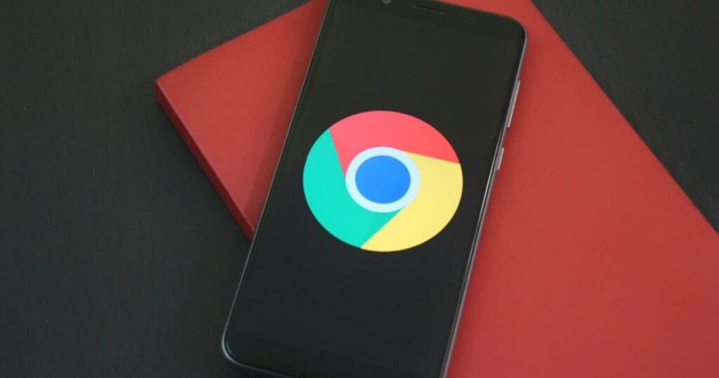 phone that shows the google chrome logo on its screen with the phone just below a red notebook