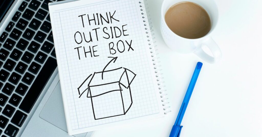 think outside the box word written on a paper with a sketch of a box, and a ballpen and a coffee on the sides