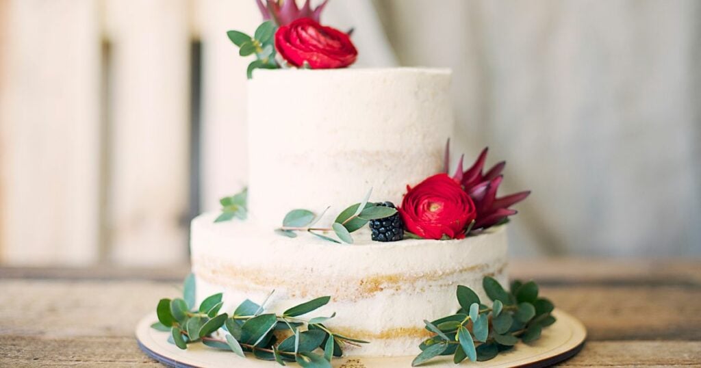 a not-so tall white wedding cake with design of a rose flowers, leaves, with a single blueberry on sides