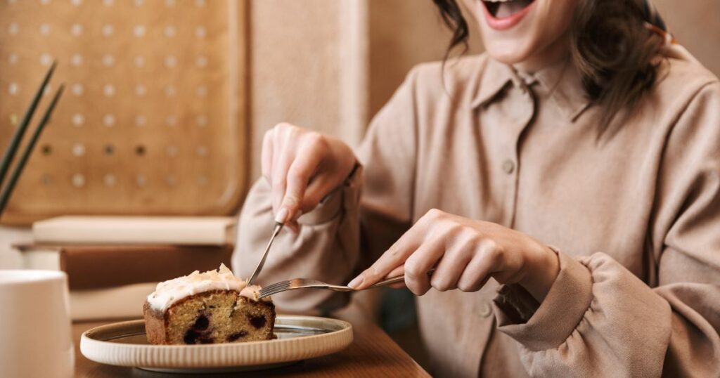 woman excitedly cutting her piece of cake with a knife and fork
