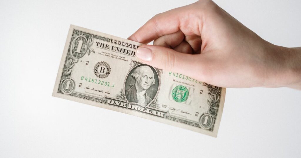 a hand holding a dollar bill with a plain, while wall or background
